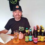 Smiling person wearing a monkey t-shirt and cap sitting at desk with laptop and beer bottles