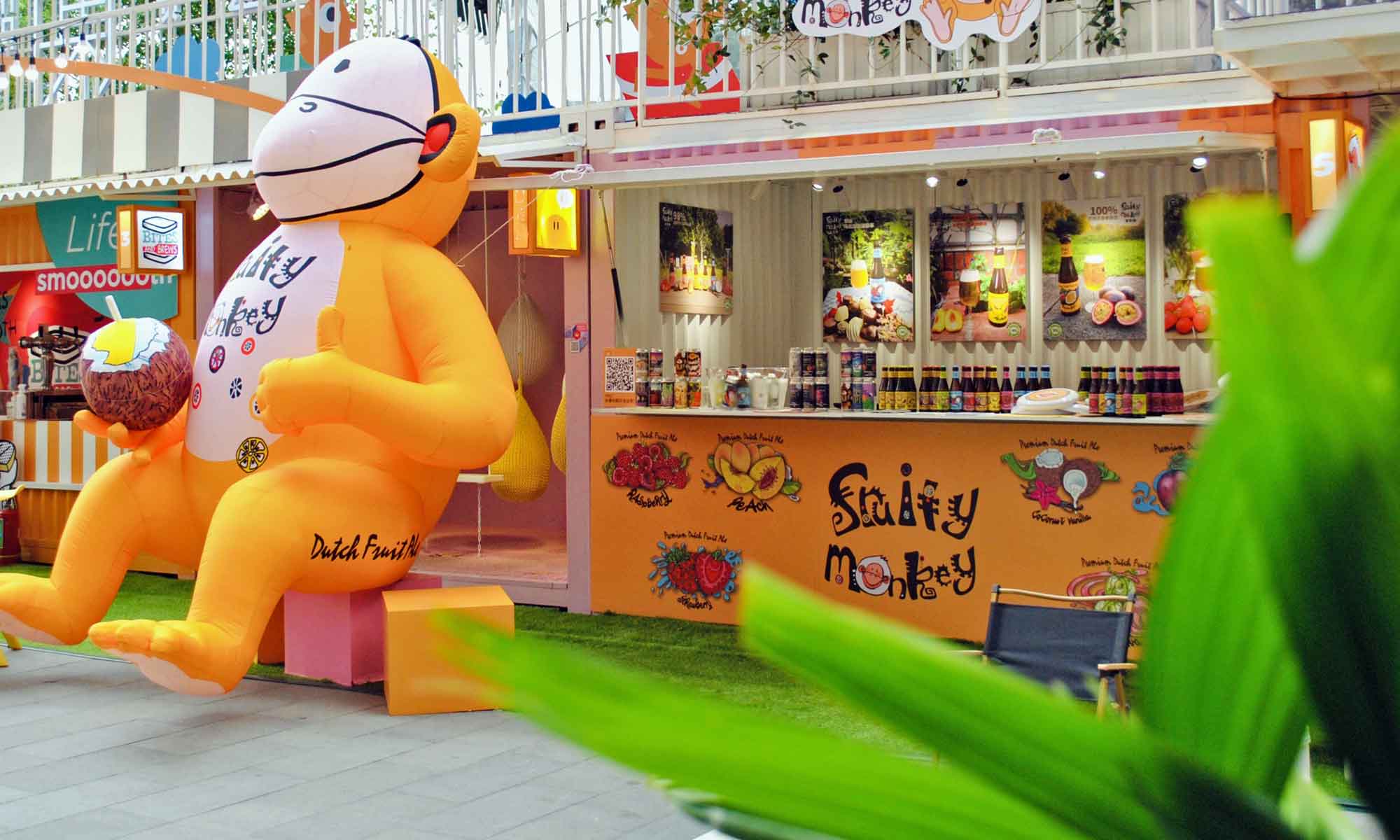 Large, inflatable yellow monkey holding a tropical fruit beer flavour beverage at a food & drink festival