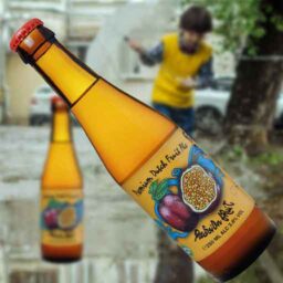 A bottle of Passion Fruit 'Fruity Monkey Beer' in front of a blurred autumn scene.