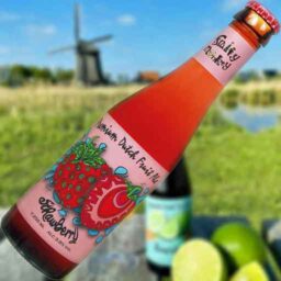 A bottle of Strawberry 'Fruity Monkey Beer' in front of a blurred summer scene.
