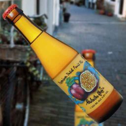A bottle of Passion Fruit 'Fruity Monkey Beer' in front of a blurred winter scene.