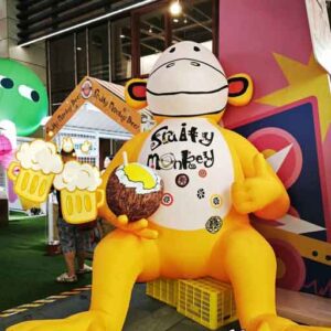 Large yellow inflatable monkey labelled Fruity Monkey holding a coconut