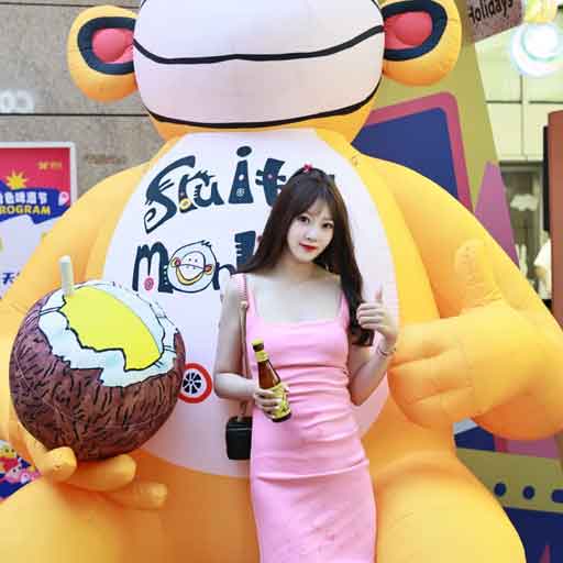 Lady holding a bottle of beer in front of a large yellow inflatable monkey, which is labelled Fruity Monkey and holds a coconut