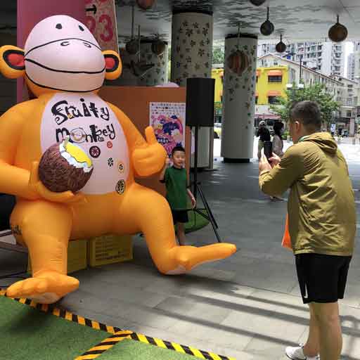 Parent taking photos of a child standing beside a large yellow inflatable monkey holding a coconut and labelled Fruity Monkey