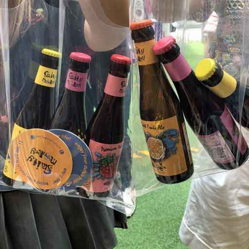 People holding colourfully labelled bottles of beer in some see-through bags
